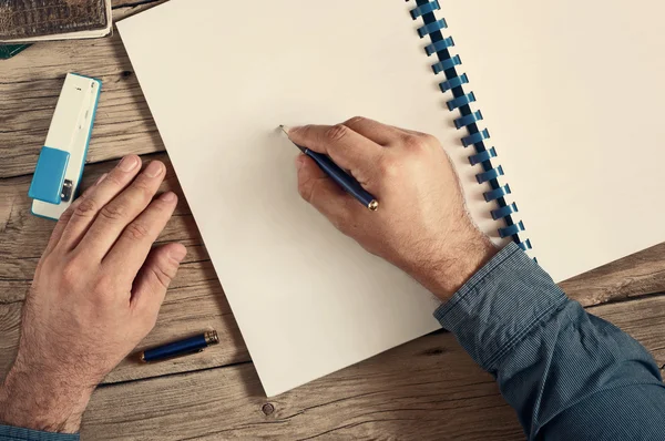 Männer schreiben in einem offenen Notizbuch mit leeren Seiten auf hölzernen Schreibtisch c — Stockfoto