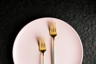 İki yeşil ve altın çatal, siyah arka planda izole edilmiş bir tabağın üstünde.