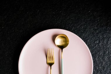 Siyah arka planda izole edilmiş pembe bir tabağın üzerinde bir çatal ve kaşık. Modern yemek..