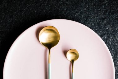 Pembe bir tabakta küçük, lüks yeşil ve altın kaşıklar. Düz ve üst manzara. kopyalama alanı. siyah arkaplan