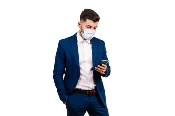 Koruyucu maskeli genç işadamı beyaz arka plandaki telefona bakıyor. Dünya salgını. Boşluğu Kopyala