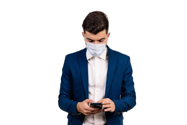Koruyucu maskeli genç işadamı beyaz arka planda cep telefonuna bakıyor. Anlaşıldı.