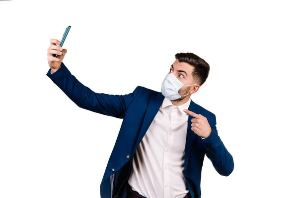 Koruyucu maskeli genç iş adamı beyaz arka planda selfie çekiyor.