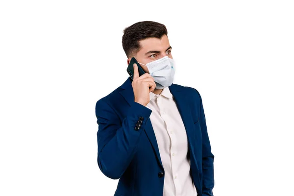 İş adamı beyaz arka planda koruyucu maske takarak cep telefonuyla konuşuyor.