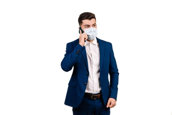 Koruyucu maskeli genç işadamı beyaz arka planda cep telefonuyla konuşuyor.