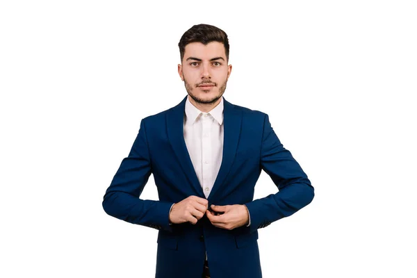 Genç adam beyaz arka plandaki kameraya bakarken ceketinin düğmelerini ilikliyor.