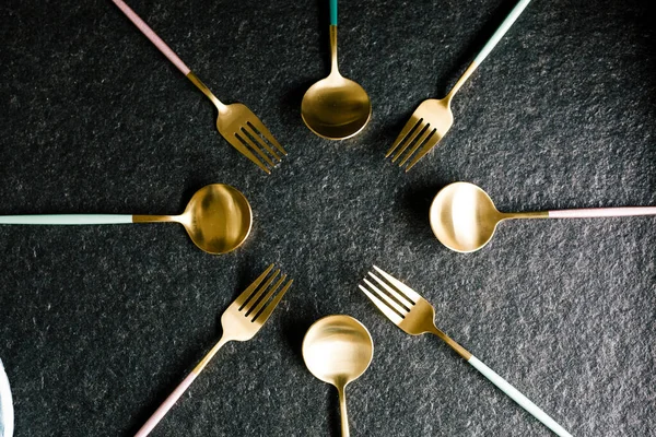 Siyah bir arkaplanda daire şeklinde dizilmiş zarif kaşık ve çatallar.