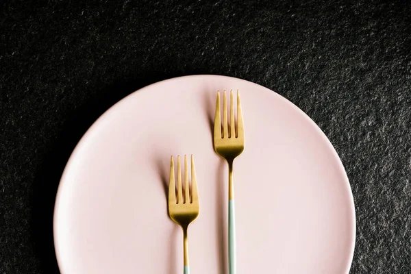 İki yeşil ve altın çatal, siyah arka planda izole edilmiş bir tabağın üstünde.