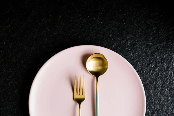 Siyah arka planda izole edilmiş pembe bir tabağın üzerinde bir çatal ve kaşık. Modern yemek..