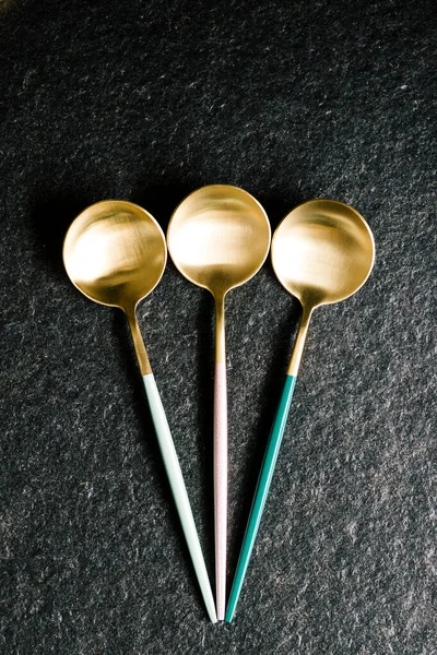 Siyah arka planda üç renkli ve lüks kaşık. Düz ve üst manzara. Modern ve zarif yemekler.