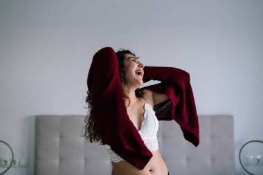 Kıvırcık esmer saçlı beyaz bir kadının portresi. Yatağın üstünde gülüyor ve dans ediyor.