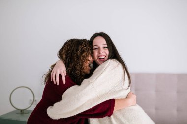 Beyaz lezbiyen çift mutlu bir şekilde yatağın üstünde sarılıyorlar. Kızlardan biri kameraya bakıp gülüyor, diğeri de omzuna yaslanıyor.