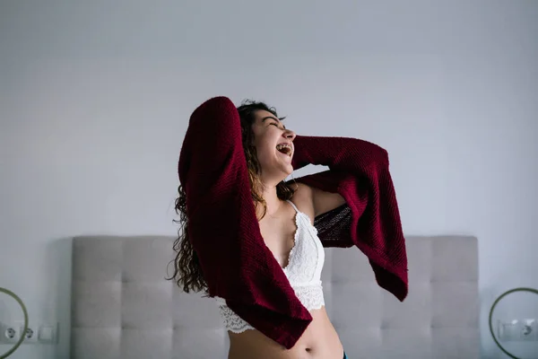 Kıvırcık esmer saçlı beyaz bir kadının portresi. Yatağın üstünde gülüyor ve dans ediyor.