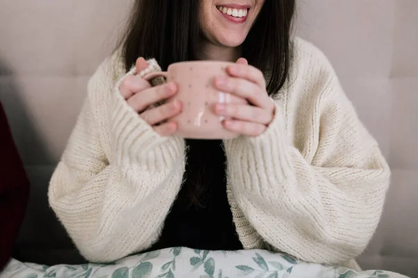 Yatakta elinde bir fincan kahve tutan beyaz bir kadının portresi. Fotoğrafta sadece ellerini ve kızın gülümsemesini görebiliyorsun. seçici odak