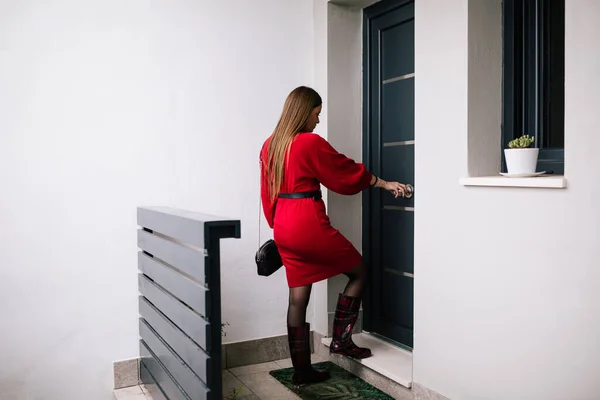 Ön kapısını açan kırmızı elbiseli genç bir kadının profil görüntüsü. Zor bir günün ardından öğrenci. İş kadını işten geliyor.