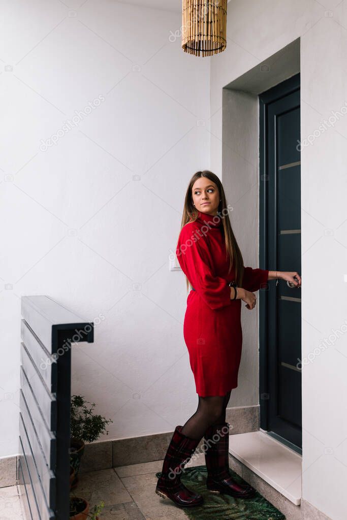 Profile view of a young woman in a red dress opening her front door. Student after a hard day. Businesswoman arriving from work