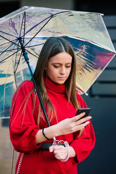 Kırmızı elbiseli genç sarı saçlı kızın portresi, şemsiye altında cep telefonuyla konuşuyor.