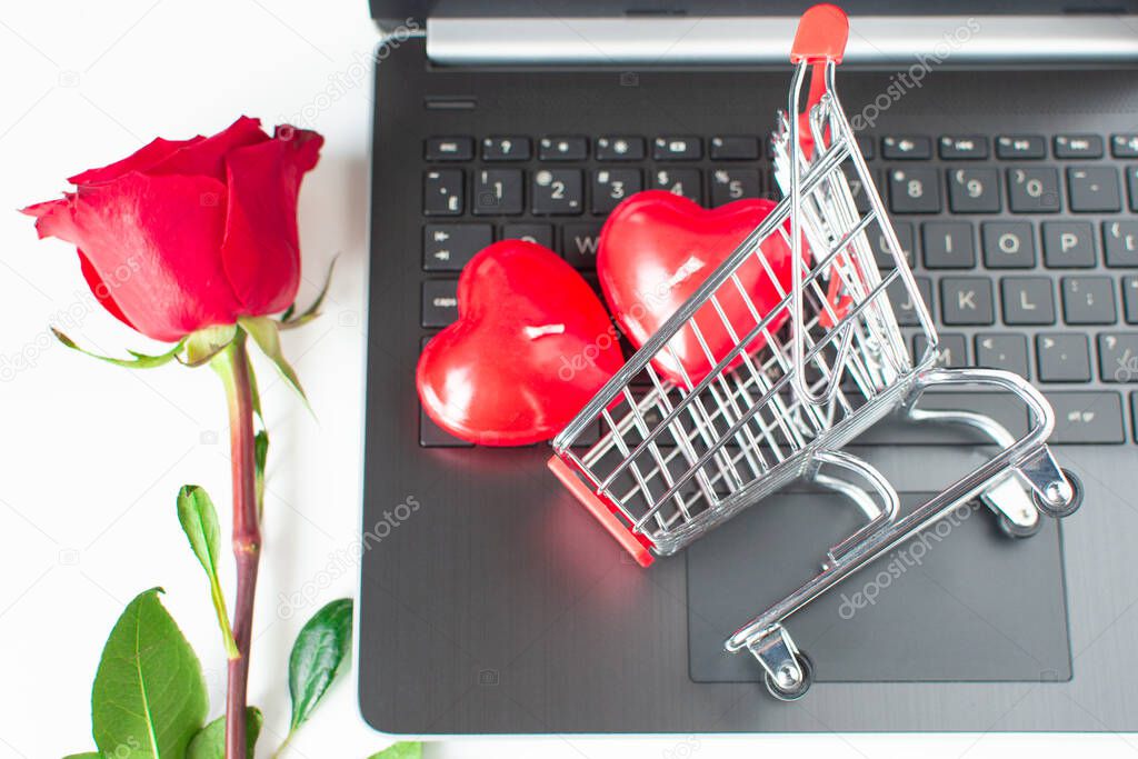 Valentine Day online Shopping. Shopping cart, laptop, red hearts, red rose. Seasonal Holiday sale. Romantic shopping for wedding, women's day, buying gifts Valentine's Day for lovers.