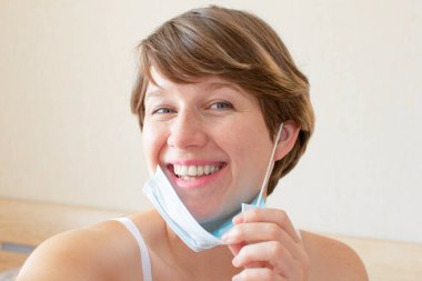 Portrait young cheerful woman taking off her medical protective mask. COVID-19 pandemic thinking concept, health. Coronavirus epidemic.
