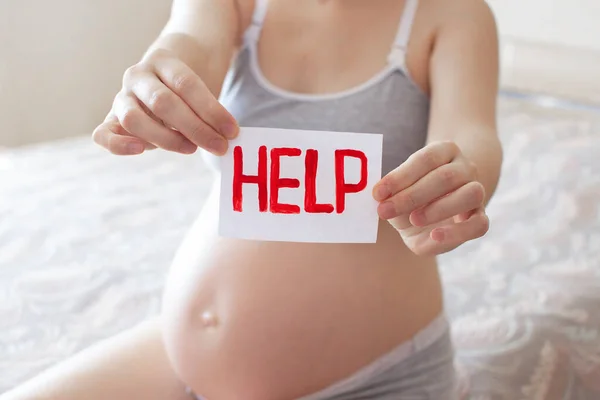 Pregnant belly with text Help sign. Concept due to the coronavirus epidemic, abortion, difficult pregnancy, motherhood, anxiety, thinking about covid-19 pandemic and illness