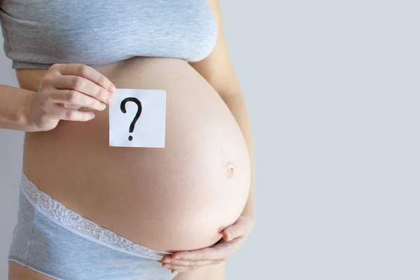 Close-up pregnant belly with question mark text. Concept to abort, toxicosis, problems of pregnant women, single mothers, AIDS and pregnancy, difficult pregnancy, motherhood, illness, anxiety