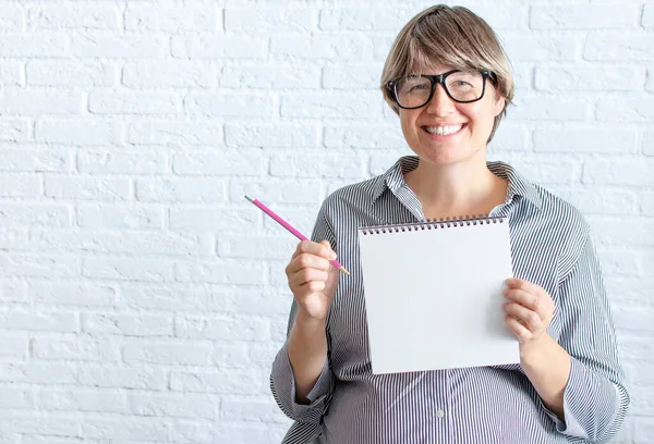 Mockup white sheet pregnant woman in office dress, holding blank white card near belly, place for text. Wish list before childbirth, planning shopping, shopping list,. Copyspace