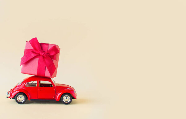 A miniature red car carrying a big gift. Holiday Valentines Day gifts, womens day, March 8, shopping. Minimal Valentines day.