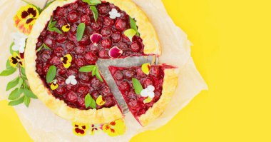 Sarı arka planda yenilebilir çiçeklerle süslenmiş vişneli turta. Kavram pişirme, yemek kitabı tarifleri, pastane afişi, kafe reklamı. Bahar, yaz ve tatil satışları. Merhaba yaz.