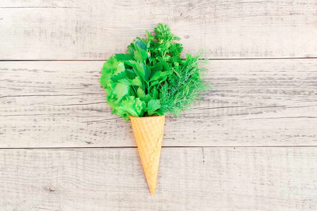 Ice cream cone with fresh herbs on a wooden background. Lettuce, parsley, dill, garlic flower. Minimal nature summer concept. Spring or summer mood minimalism. Copyscape, flatlay, top view. Close up