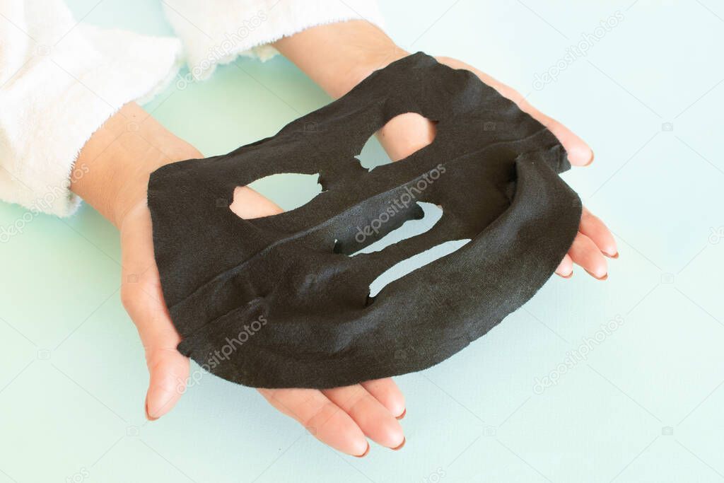 Anti age concept. Senior woman holds and applies a black cosmetic mask to her face. Mature woman spa treatment. Beauty spa treatment. Plastic surgery clinic, new senior, cosmetology