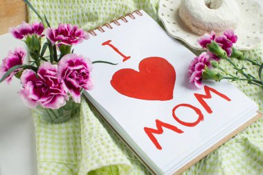 Pembe arka planda Anneler Günü tebrik kartı. Annemi sevdiğimi mesaj at. Kahvaltı, karanfil, bağış, hediye ve çocuk tarafından annem için yapılmış bir kartpostal..