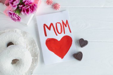 Beyaz arka planda Anneler Günü tebrik kartı. Kahvaltı, karanfil hediyesi ve çocuk tarafından annem için yapılmış bir kartpostal..