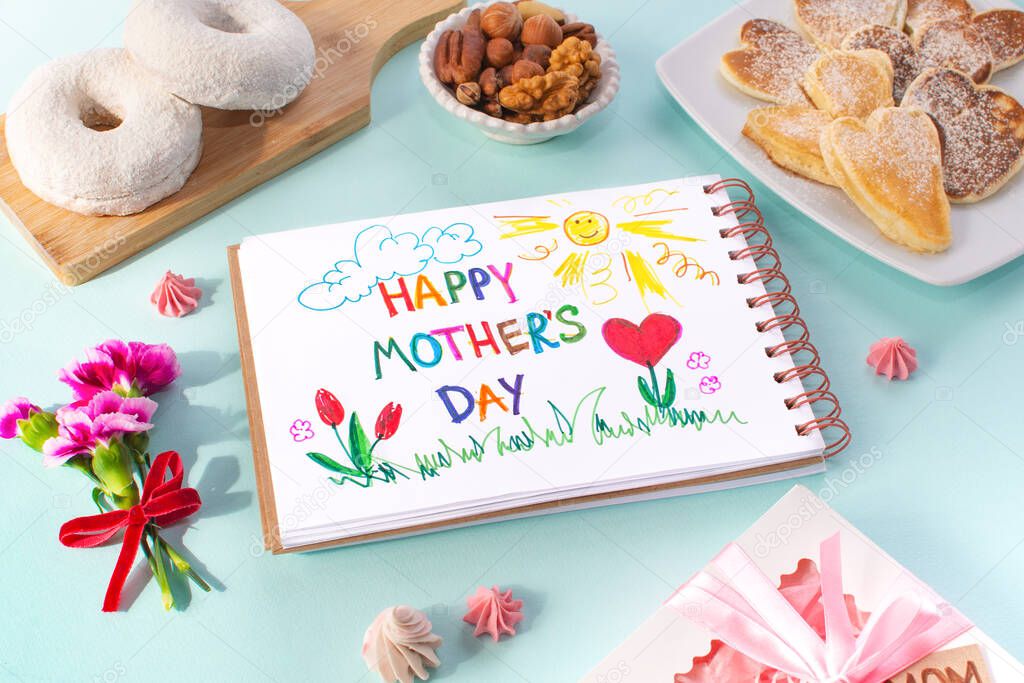 Mothers day breakfast card made by a child. Text Happy Mother day. On a colored background. Pancake in the form of hearts, donat, nuts, carnation, gift and a postcard made by the kids for mum.