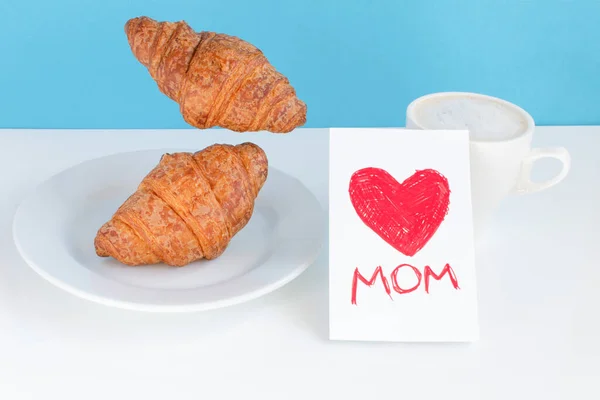 Levitating food Mothers day breakfast. Flying croissantst and a cup of coffee on a blue background. Modern breakfast balance still life concept food.