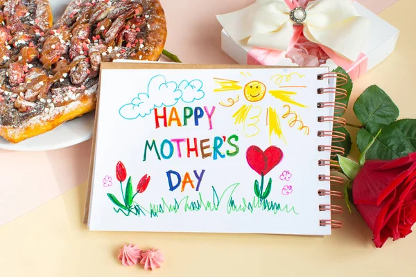 Szczęśliwego Dnia Matki martwa natura. Śniadanie dla mamy słodka pizza, czerwona róża, prezent i rysunek dłoni w albumie przygotowanym przez dziecko dla mamy. Tekst Szczęśliwego Dnia Matki. — Zdjęcie stockowe