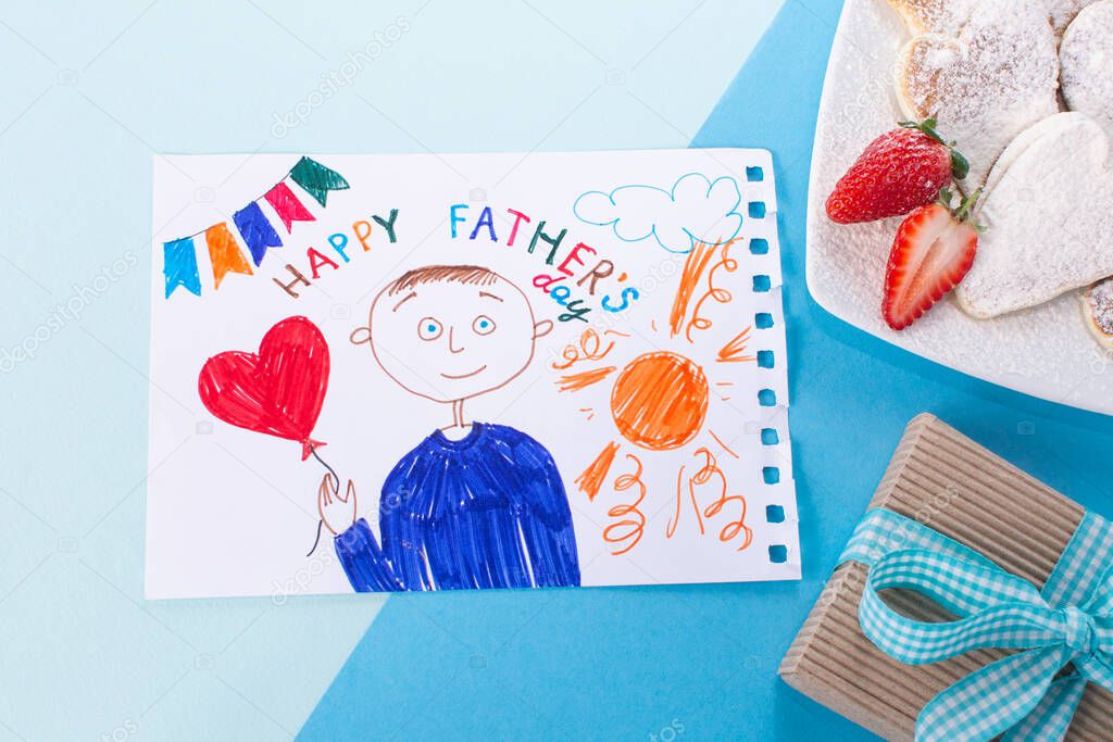Father day Breakfast pancakes, gift on a blue minimal background. Childs drawing of her dad. Concept Happy Fathers Day flat lay