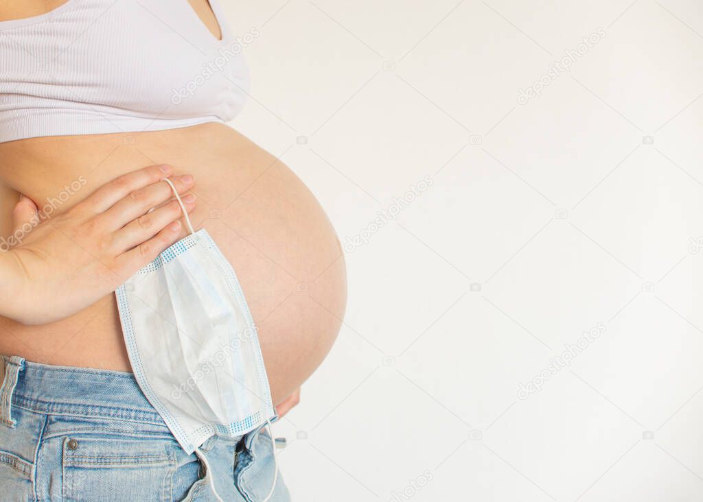 Pregnant belly with medical protective mask on light background. Concept pregnancy in coronavirus epidemic, covid-19 pandemic, problems of pregnancy, toxicosis, abortion, risk of miscarriage, illness