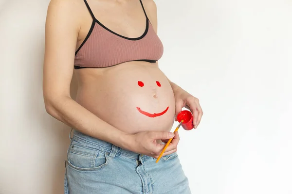 Boyayla çizilmiş gülüşü olan hamile bir göbekli kız. Hamile kadın, elinde boyalarla eğleniyor. Hamile bir kızın bebek beklemesinin neşe ve mutluluğu. Kopyalama alanı