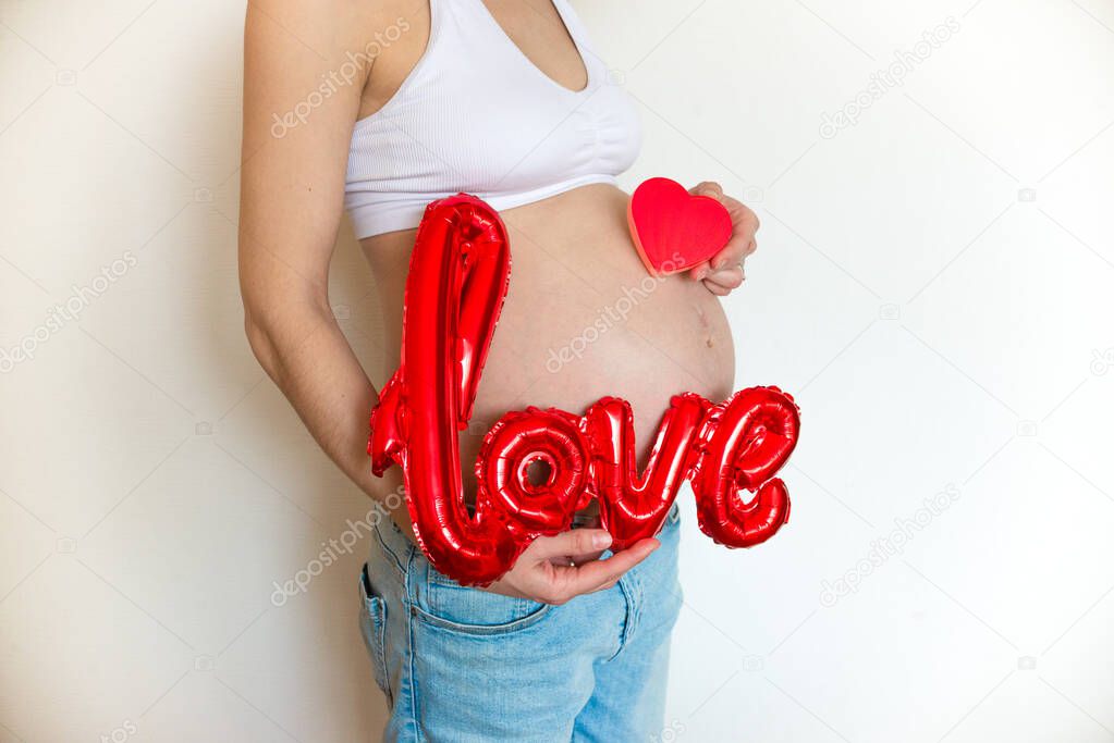 Pregnant belly with balloon love and red heart on a light background. The joy and happiness of motherhood. Copyspace