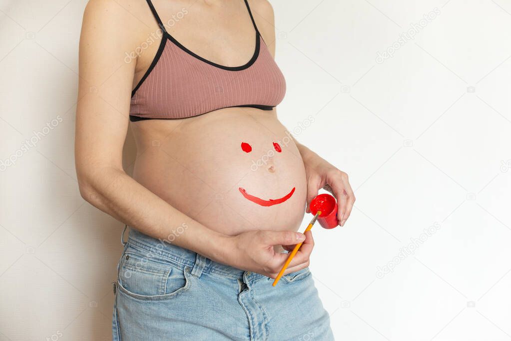 Pregnant belly girl with a smile drawn by paint. The pregnant woman is having fun with paints in her hands. The joy and happiness of motherhood pregnant girl in anticipation of the baby. Copyspace
