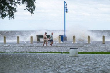 NEW ORLEANS, LA - SEPTEMBER 15, 2020: Two men walking along flooded Lakeshore Drive and Lake Pontchartrain during Hurricane Sally storm surge clipart