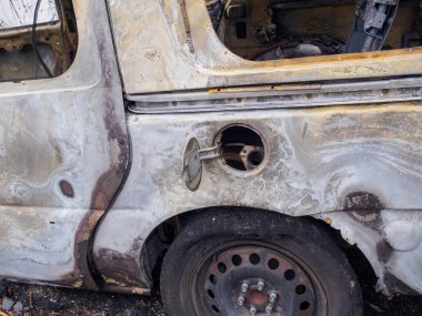 Terk edilmiş ve yanmış arabanın yolcu tarafında benzin deposu, erimiş lastik ve arka paneli görünüyor.