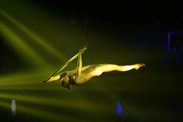 Esnek genç kadın, hava çemberinde performans sergiliyor, sarı ışık, hava sirkinde esnek bölünme, hava sirki gösterisi.