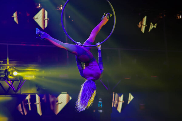Flexible sexy athletic woman, aerial acrobatic hoop performance, women upside down on aerial hoop with high heels backlit in yellow light, air circus show