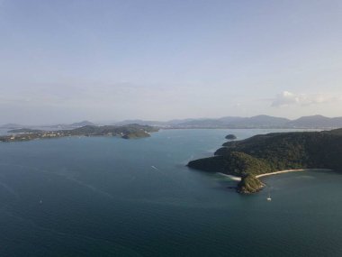Tropikal ada, gün batımında gökyüzünden, dağdan, küçük serbest plajdan, Phuket şehrinin ve dağların arkasından. Seyahat konsepti