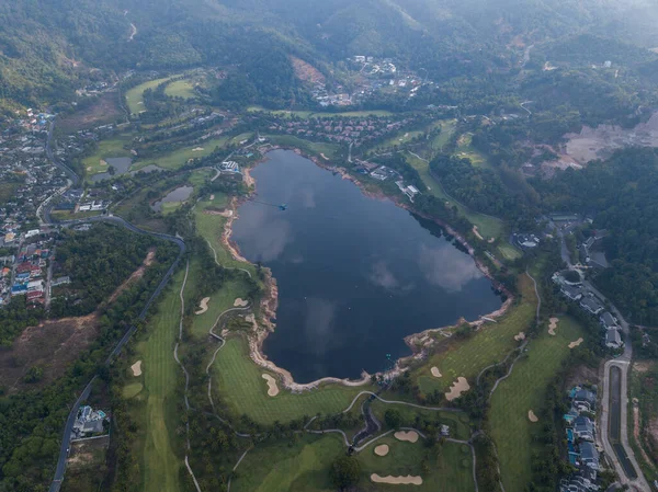 Şafak vakti evlerle ve dağlarla çevrili bir golf sahasında bulunan güzel göl. İnsansız hava aracının fotoğrafı. Gölde, gökyüzünün yansıması. Seyahat ve golf reklamı için harika bir geçmiş..