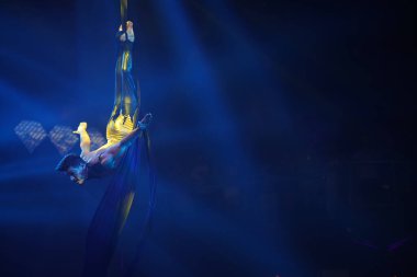 Brezilyalı güçlü seksi adam mavi ışıklardaki hava ipekleriyle performans sergiliyor. Spor salonu ve yaşam tarzı konsepti. Siyah arka plan. Havadan ipekle jimnastikçi baş aşağı duruyor. Erkek vücudu