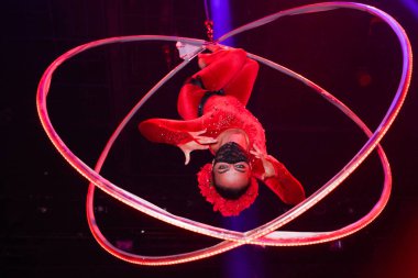 Esnek genç bir kadın, hava çemberinde performans sergiliyor. Hava çemberinde esnek duruyor. Hava sirki gösterisi, mavi ve kırmızı ışık. Esnek kadın jimnastikçi potada baş aşağı duruyor. Gece kulübü performansı