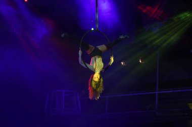 Esnek genç kadın hava çemberinde performans sergiliyor, hava çemberinde esnek duruyor, hava sirki gösterisi, sarı mavi mavi ışık. Esnek kadın jimnastikçi potada baş aşağı duruyor. Gece kulübü performansı