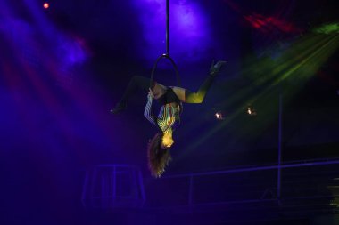 Esnek genç kadın hava çemberinde performans sergiliyor, hava çemberinde esnek duruyor, hava sirki gösterisi, sarı mavi mavi ışık. Esnek kadın jimnastikçi potada baş aşağı duruyor. Gece kulübü performansı